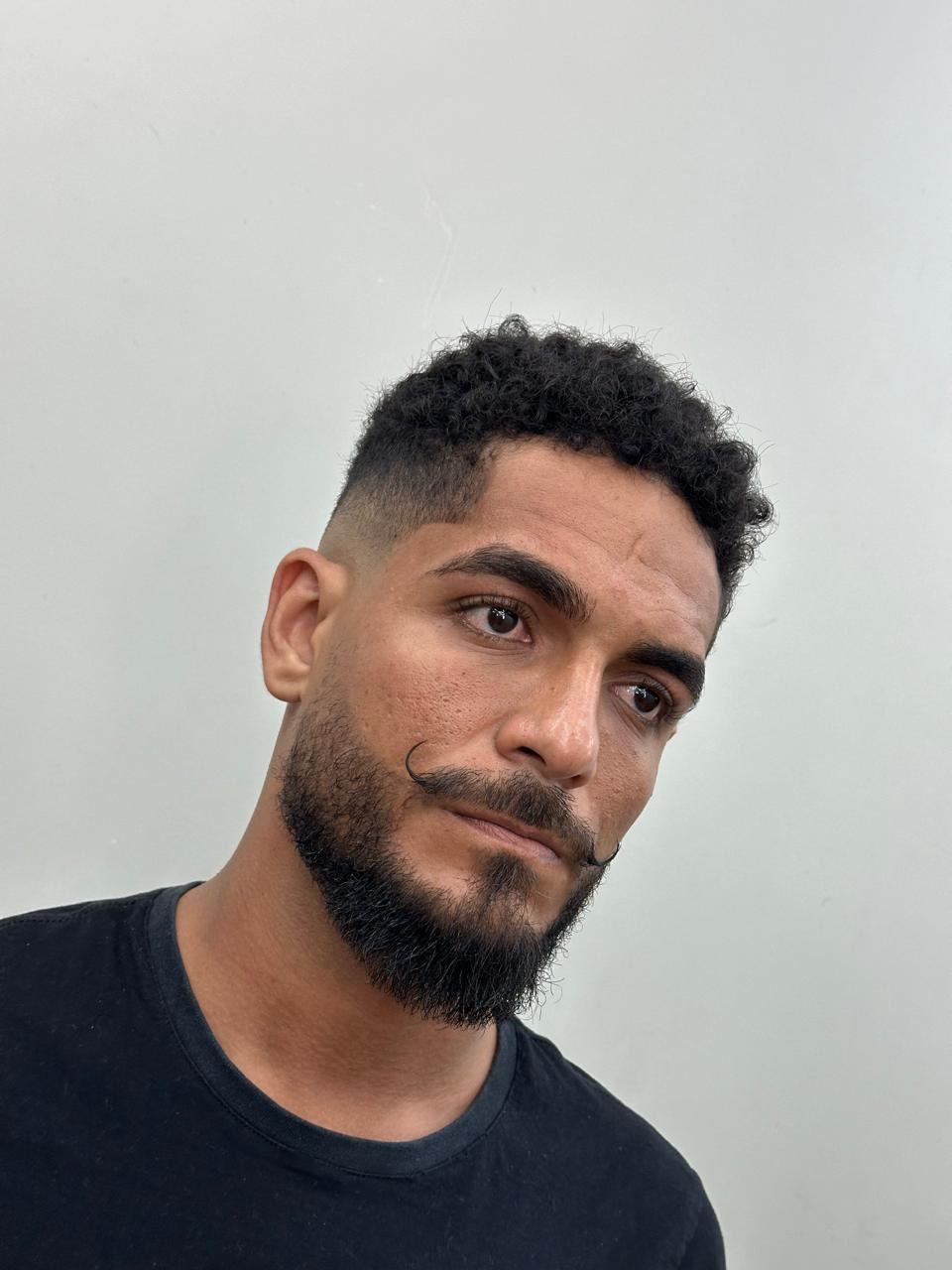 Cliente com cabelo cacheado, degradê baixo e bigode modelado